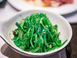 Typical Japanese dish of algae with sesame and soy sauce, in a ceramic bowl on a table.