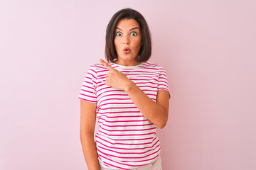 Young beautiful woman wearing striped t-shirt standing over isolated pink background Surprised pointing with finger to the side, open mouth amazed expression.