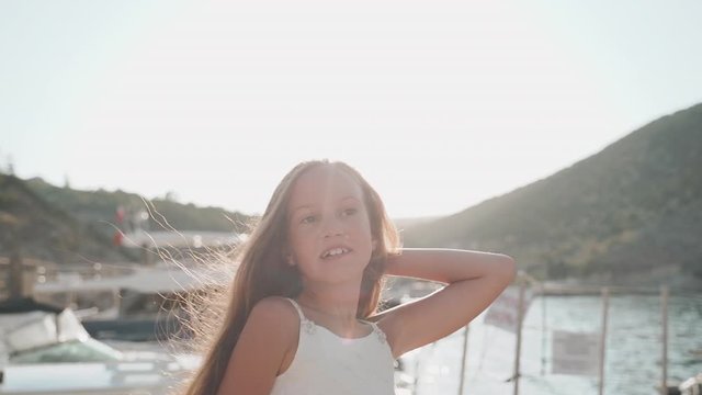 Child girl standing against sunny port with boat