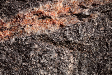 Abstract blurred natural background. Black with pink-orange rough surface of granite. Design and construction concept.