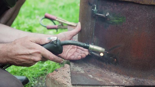 Craftsman's hands close up. Worker welding metal door of a stove in a backyard.