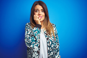 Young beautiful woman wearing a jacket standing over blue isolated background looking stressed and nervous with hands on mouth biting nails. Anxiety problem.