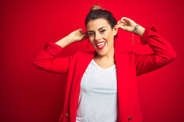 Young beautiful business woman standing over red isolated background Smiling pulling ears with fingers, funny gesture. Audition problem