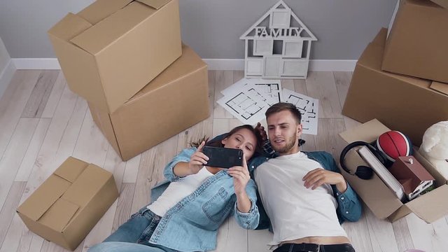 Young happy couple posing on smartphone camera with boxes on the background.