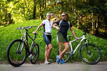 Obraz premium Smiling man and woman with bicycles stand near a green hill.