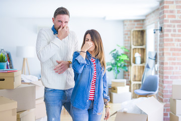 Young beautiful couple standing at new home around cardboard boxes smelling something stinky and...