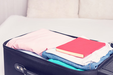 Open suitcase with clothes and notebook, close up, cropped image, toned