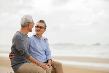 Happy asian senior couple have fun and enjoy at the beach, senior man and woman hugging while sitting on the beach Retirement Lifestyle Healthy Travel Vacation Concept