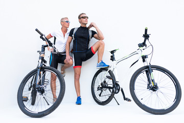 Athletic man and woman with bicycles holding hands posing on a light background.