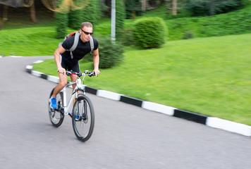 A man rides a bicycle along a path in a park, out of focus.