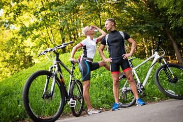 Plakat Athletic man and woman with bicycles posing in the park on a background of green knoll.
