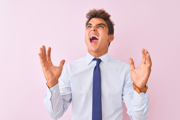 Young handsome businessman wearing shirt and tie standing over isolated pink background crazy and mad shouting and yelling with aggressive expression and arms raised. Frustration concept.