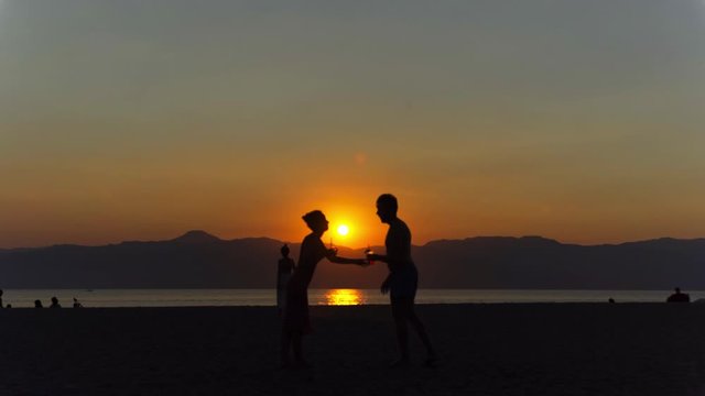 Young couple enjoying beautiful orange sea sunset on the beach. Romantic man and woman dancing and looking at each other. Silhouette of couple in love at sea sunset. Concept of love and happiness