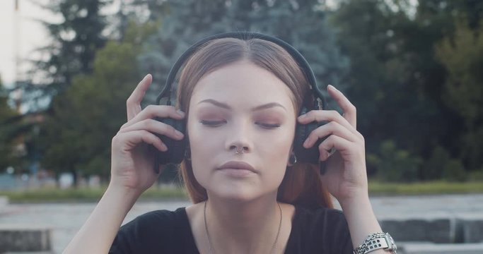 Beautiful female model listens to music on black bluetooth over the ear headphones