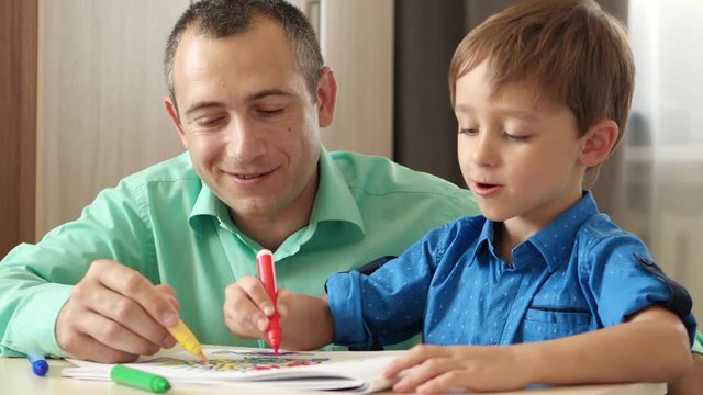 Happy family. A father teaches his son to draw sitting at a table. Dad and child depict their dream on paper with colored markers.