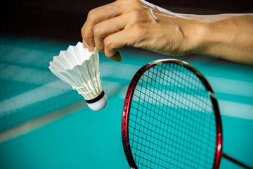 Hands of Badminton player holding racket and serving shuttlecock with blur Badminton court background.