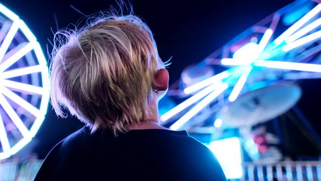 Toddler staring up at parachute carnival ride. Static. Slowmo. Blur background