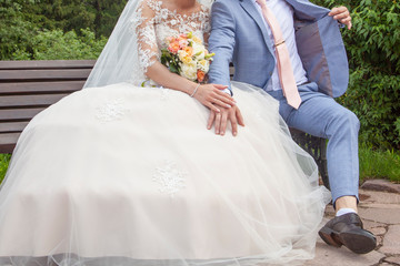 Bride and groom. The bride in a white wedding dress and a man in a suit. The bride and groom on the street in the park. Hands of the bride and groom next to each other.