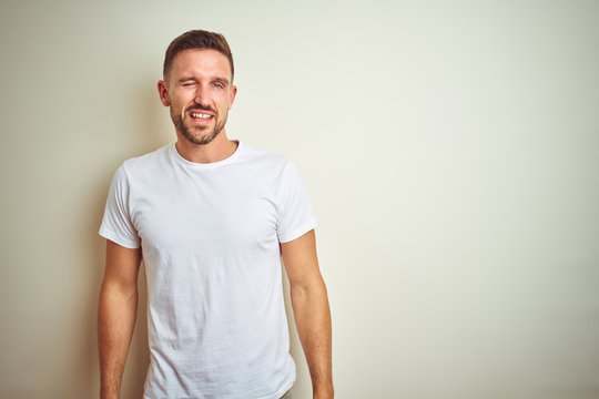 Young handsome man wearing casual white t-shirt over isolated background winking looking at the camera with sexy expression, cheerful and happy face.