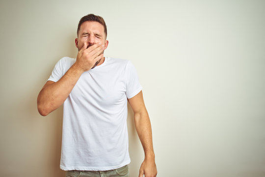 Young handsome man wearing casual white t-shirt over isolated background bored yawning tired covering mouth with hand. Restless and sleepiness.