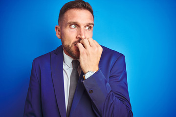 Close up picture of young handsome business man over blue isolated background looking stressed and nervous with hands on mouth biting nails. Anxiety problem.