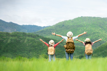 Happy tourist asian girl with two little girl standing hands up on  meadow with mountain background at natural park, travel education environment lifestyle concept