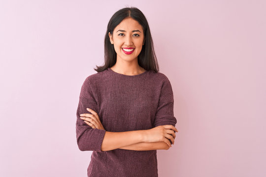 Young chinese woman wearing purple sweater standing over isolated pink background happy face smiling with crossed arms looking at the camera. Positive person.