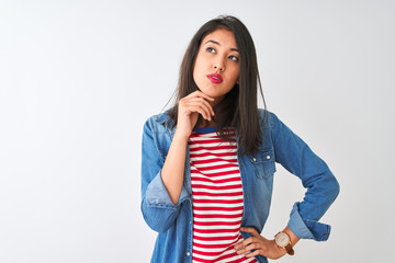 Young chinese woman wearing striped t-shirt and denim shirt over isolated white background with hand on chin thinking about question, pensive expression. Smiling with thoughtful face. Doubt concept.