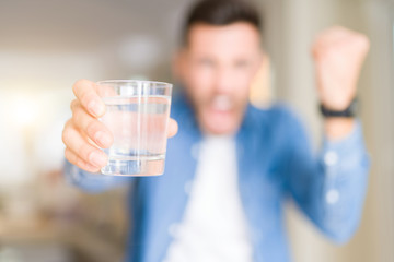Young handsome man drinking a glass of water at home annoyed and frustrated shouting with anger, crazy and yelling with raised hand, anger concept