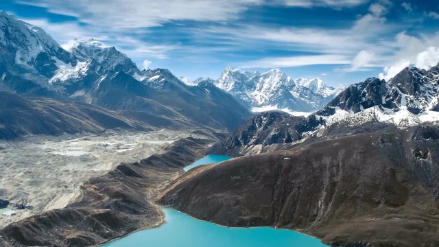 Calm Blue Gokyo Lake surrounded by bare rocky hills against high mountains with snow on slopes upper view. Travel, landscape, holiday, recreation. Himalaya, Nepal. Slow motion, parallax, time lapse 4K
