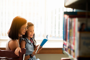 Happy Asia woman  in eyeglasses reading a book with her daughter at a bookstoreor library , Relaxing lifestyle  healthy family  education concept