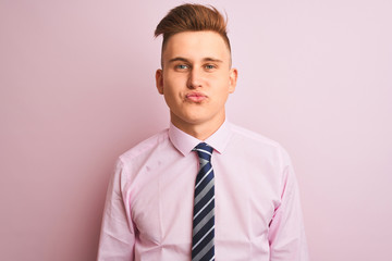 Young handsome businessman wearing shirt and tie standing over isolated pink background looking at the camera blowing a kiss on air being lovely and sexy. Love expression.