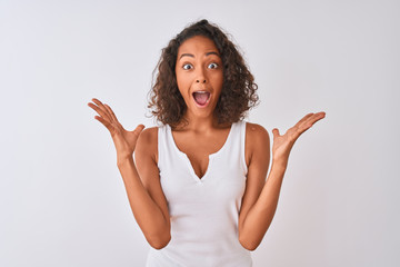 Young brazilian woman wearing casual t-shirt standing over isolated white background celebrating crazy and amazed for success with arms raised and open eyes screaming excited. Winner concept