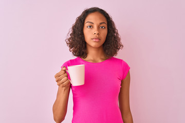 Young brazilian woman drinking cup of coffee standing over isolated pink background with a confident expression on smart face thinking serious