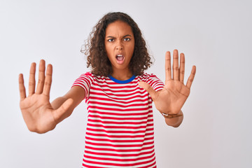 Young brazilian woman wearing red striped t-shirt standing over isolated white background doing stop gesture with hands palms, angry and frustration expression