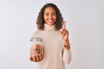 Young brazilian woman holding jar of cookies standing over isolated white background surprised with...