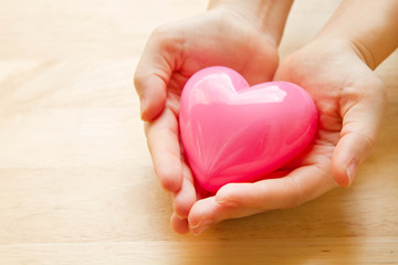 Hands holding pink heart with wooden background