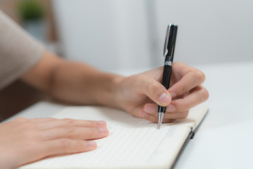 Close up hands of person writing note to notebook pages.