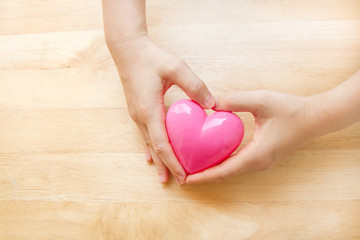 Hands holding pink heart with wooden background