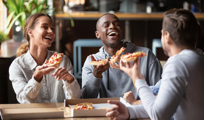 Joyful multicultural friends laughing sharing takeaway pizza meal together