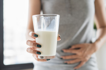 lactose intolerance concept. Woman holding a glass of milk and having a stomachache.