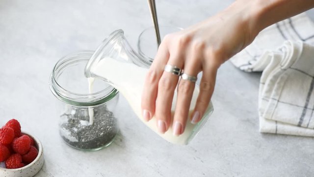 Chia pudding step by step recipe. Woman's hand add almond milk to jar with chia seeds. Healthy vegan and vegetarian food