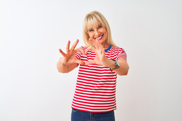 Middle age woman wearing casual striped t-shirt standing over isolated white background smiling in love doing heart symbol shape with hands. Romantic concept.