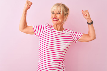Middle age woman wearing striped t-shirt standing over isolated pink background showing arms...