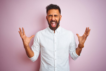 Fototapeta premium Young indian businessman wearing elegant shirt standing over isolated pink background celebrating mad and crazy for success with arms raised and closed eyes screaming excited. Winner concept