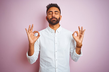Young indian businessman wearing elegant shirt standing over isolated pink background relax and smiling with eyes closed doing meditation gesture with fingers. Yoga concept.
