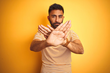 Young indian man wearing t-shirt standing over isolated yellow background Rejection expression...