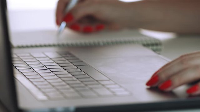 Woman hands with red manicure using laptop to work study and writing on paper with a pen. Business, financial, trade stock maket and social network concept.