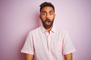 Young indian man wearing casual shirt standing over isolated pink background afraid and shocked...