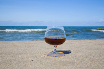 Cognac in a glass on the shore of the blue sea. Stay with alcohol in the South